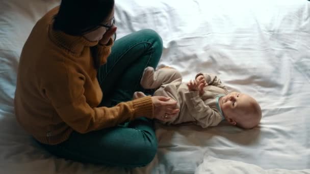 Madre cariñosa jugando con el bebé en la cama. Niño recién nacido sonriente madre — Vídeos de Stock