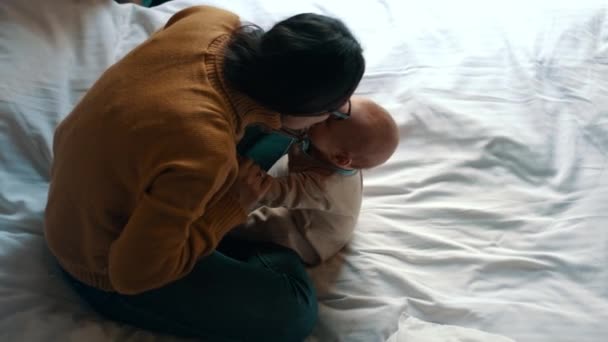 Gülüyor ve küçük bebeği ile beyaz yatakta oynayan kadın. Anne ve çocuk — Stok video