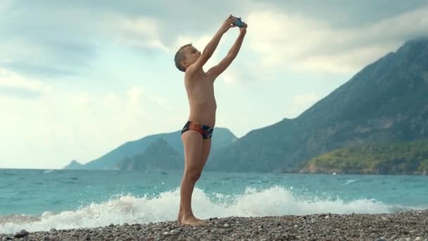 Niño haciendo foto selfie en el teléfono móvil en la playa del mar en las vacaciones de verano — Vídeo de stock