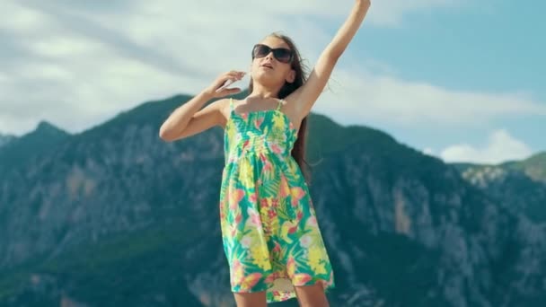 Chica cantando con teléfono en las montañas. Chica joven escuchando música en el teléfono móvil — Vídeos de Stock