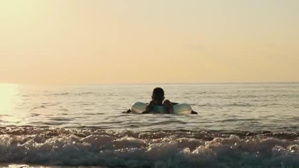 Jongen drijven op rubberring op zee bij zonsondergang. Kind zwemmen met rubber cirkel — Stockvideo