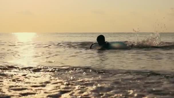 Little boy learning to swim on inflatable circle in sea during sunset — Stock Video