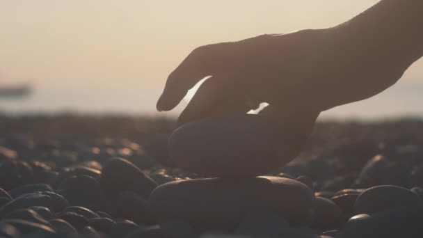Жінка рука будує вежі з гальки на пляжі на заході сонця. Релаксація на пляжі — стокове відео