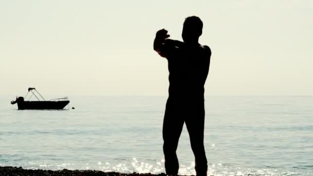 Silhouette de l'homme faisant des exercices matinaux sur la plage de la mer — Video