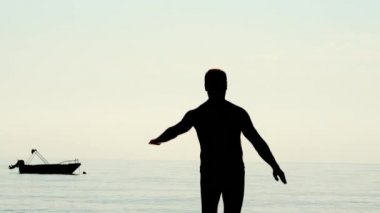 Siyah erkek siluet plajda fiziksel egzersizleri yapıyor. Denize yakın oturan adam