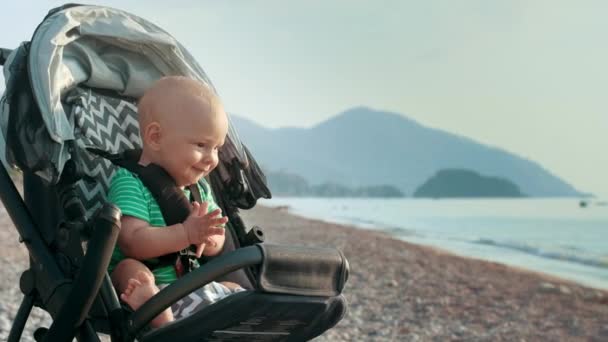 Happy baby handen klappen in de kinderwagen op zee strand. Jongetje handen klappen — Stockvideo