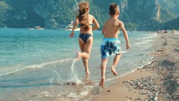 Boy and girl running at sea beach. Children fun on beach at summer vacations — Stock Video