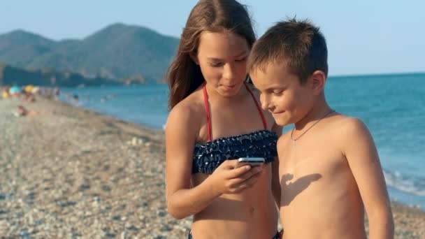 Kinder suchen Foto auf dem Smartphone am Meeresstrand. Junge mit Mädchen überprüft Foto — Stockvideo