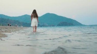 Küçük kız yavaş yavaş sahil yürüyüş. Deniz dalgaları üzerinde yürüyüşe çocuk