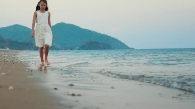 Üzgün kız yalnız ağır çekimde deniz sahilinde yürüyüş. Düşünceli kız rahat yürüyüş