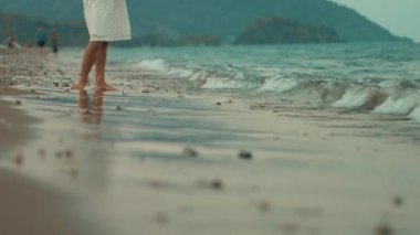 Kadın ayakları üzerinde deniz plaj gün batımında. Genç kız denizde dalgalar ayakta. Kız ayaklarınızı deniz dalgaları ile yıkadım. Çocuk kumsalda yaz tatillerini sakin ol