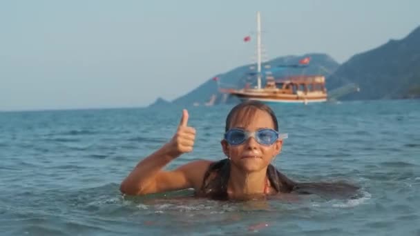 Menina emergindo do mar e mostrando polegar. Criança alegre que toma banho no mar — Vídeo de Stock