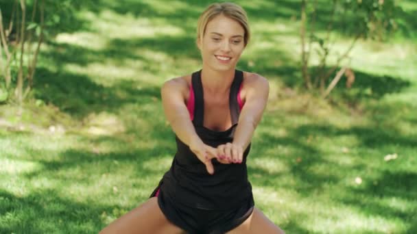 Mulher sorridente esticando as pernas antes de academia de fitness no parque. Mulher fitness — Vídeo de Stock
