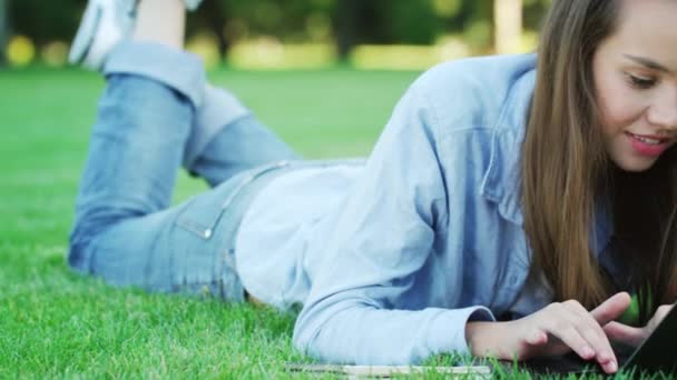 Lachende vrouw liggend op gras en typen op laptop in zomer park — Stockvideo