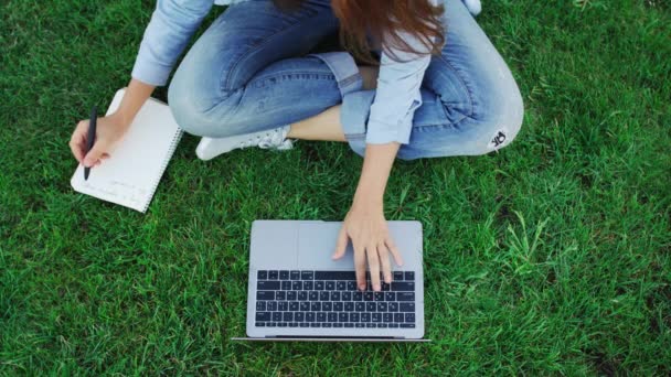 Estudante mulher trabalhando no computador portátil e escrevendo notas no notebook no parque — Vídeo de Stock