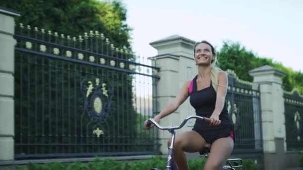 Mujer feliz montando bicicleta y saludando de la mano en el parque. Mujer disfrutando bicicleta — Vídeo de stock