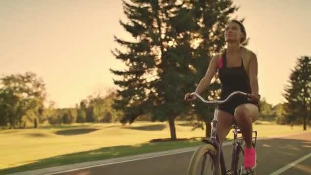 Женщина на велосипеде в летнем парке на фоне золотого заката — стоковое видео