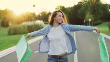 Alışveriş çantası günbatımında sokakta yürürken tutan mutlu kadın