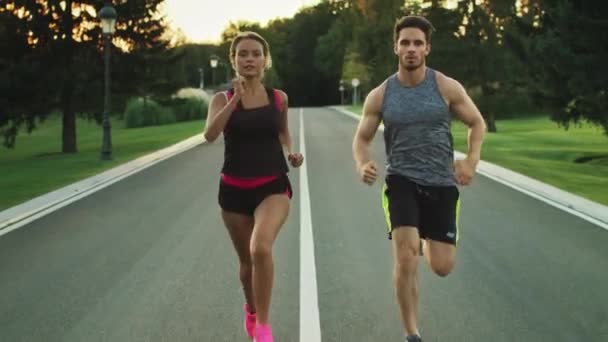 Deportistas corriendo juntos en el parque. Pareja joven trotando en el entrenamiento al aire libre — Vídeos de Stock