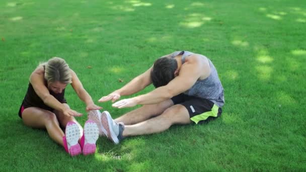 Sportovní dvojice roztáhnout cvičení na zelené trávě v letním parku — Stock video