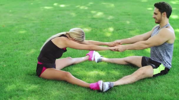 フィットネス トレーナー ヘルプ若い女性ウォーム アップの公園でのトレーニングで脚をストレッチします スポーツ カップル ストレッチと一緒に手します 朝フィットネス屋外 — ストック動画