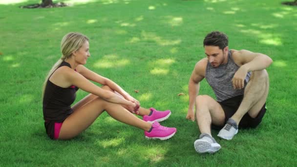 L'atleta uomo aiutare la giovane donna alzarsi dal prato verde. Lavoro di squadra per gli sportivi — Video Stock