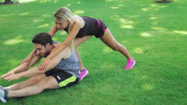 Mujer entrenador deportivo ayuda a fitness hombre estirar las piernas en el parque de verano — Vídeo de stock