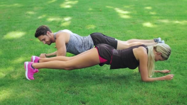 Fitness couple man and woman training plank exercise on grass in summer park — Stock Video