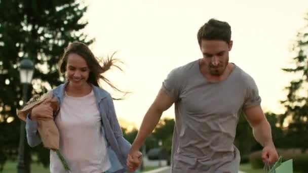 Pareja feliz con flores corriendo en el parque de verano. Pareja enamorada — Vídeos de Stock