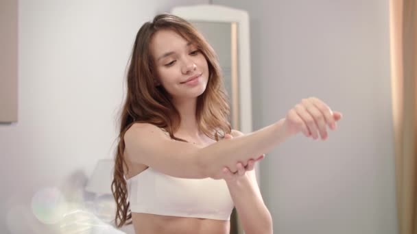 Soin de la peau des femmes le matin. Fille heureuse appliquant lotion pour le corps sur les mains à la maison — Video