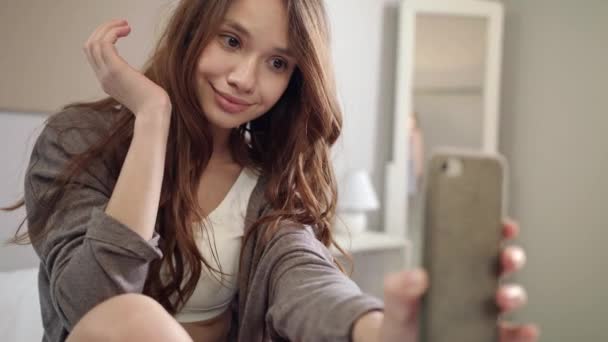 Молодая женщина делает селфи фото на мобильном телефоне в спальне — стоковое видео