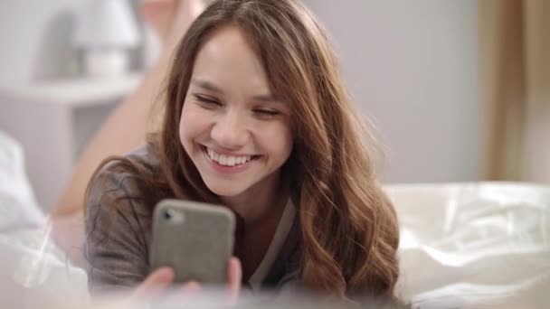 Mujer joven tomando foto selfie en el teléfono móvil en la cama. Chica bonita posando — Vídeos de Stock