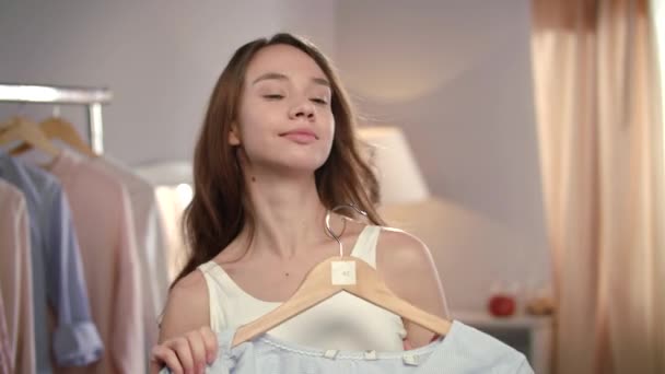 Щаслива дівчина намагається одягнутися в домашній гардероб. усміхнена жінка вибирає літнє плаття — стокове відео