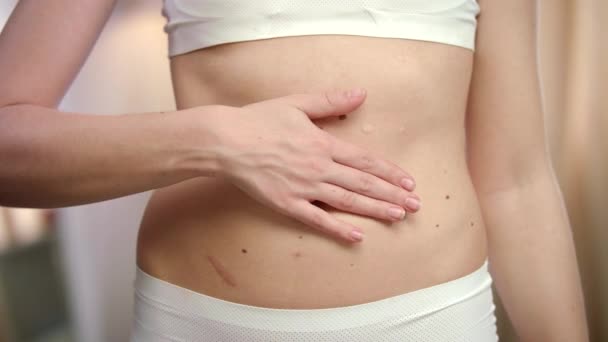 Mano de mujer aplicando crema corporal en el abdomen. Cuidado de la piel del vientre de mujer — Vídeos de Stock