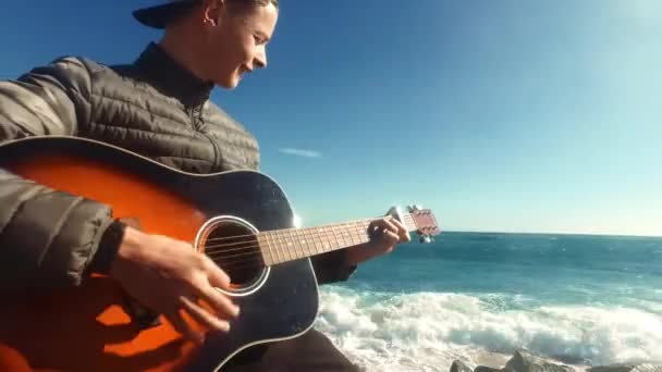 Niño feliz tocando la guitarra acústica en la playa. Joven músico toca la guitarra — Vídeo de stock