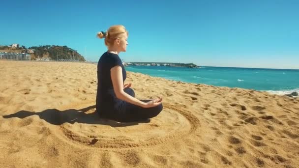 Молодая женщина медитирует в позе лотоса на морском пляже. Спортивная девушка практикующая йогу — стоковое видео