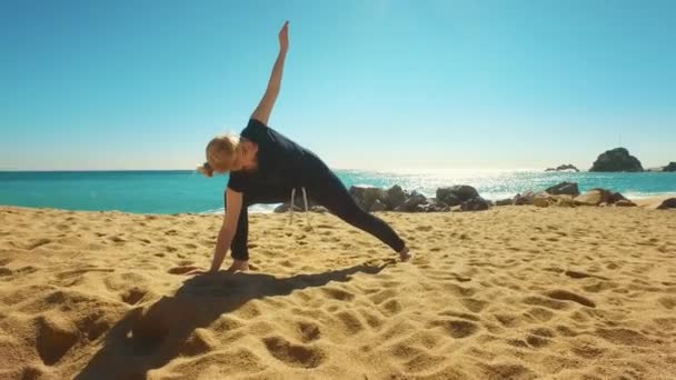 Женщина практикует йогу асана на морском пляже. Подходящая девушка делает упражнения на гибкость — стоковое видео