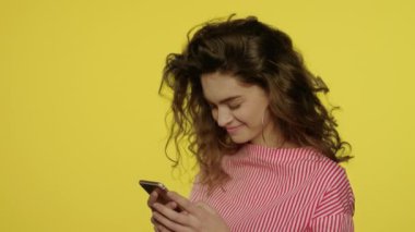 Sarıda cep telefonu kullanan genç bir kadın. Cep telefonunda mesaj yazan kadın