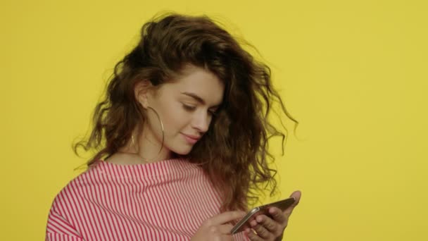 Mujer sonriente haciendo gestos en el teléfono móvil. Mujer joven mirando foto en el teléfono inteligente — Vídeos de Stock