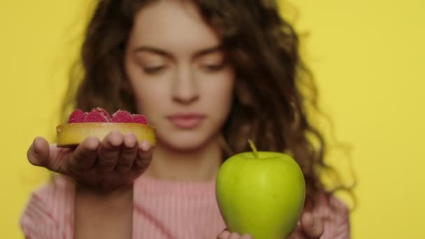 Mujer joven sosteniendo fruta de manzana y pastel de bayas sobre fondo amarillo — Vídeos de Stock