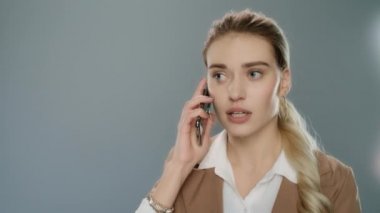 Sinirli iş kadını gri arka planda cep telefonunu arıyor.