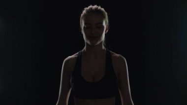 Siyah arka planda elinde dambıllarla poz veren formda bir kadın. Spor kadını.