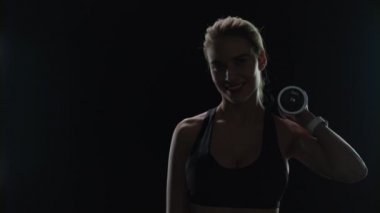 Spor salonunda omuzlarında dambılla gülümseyen spor kadını. Spor modeli gülümsüyor