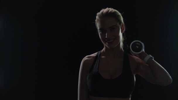 Sport kvinna ler med hantel på axeln i gymmet. Fitness modell leende — Stockvideo
