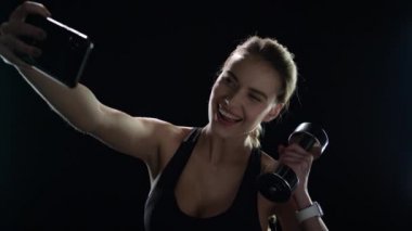 Spor kadını spor salonunda cep telefonuyla selfie çekiyor.