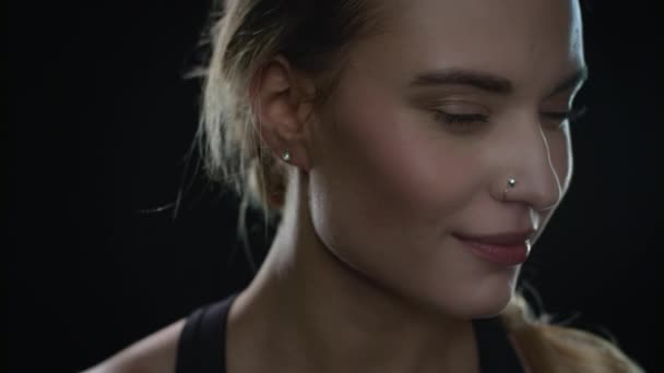 Mladá žena se směje v černém studiu. Detailní záběr fit dívka s piercing v nose — Stock video