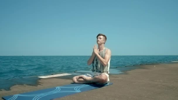 Hombre sentado junto al mar en posición de loto y luego de pie sobre su cabeza. Hombre haciendo yoga — Vídeo de stock