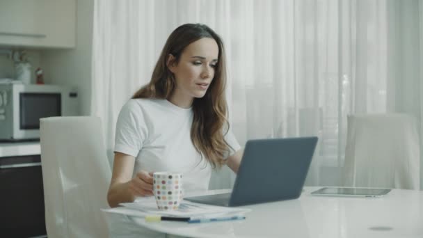 Mujer usando computadora portátil en la cocina. Retrato de mujer de negocios viendo noticias — Vídeos de Stock