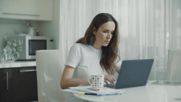 Vermoeide vrouw met laptop computer thuis. Ernstige vrouw drinken thee op de keuken — Stockvideo