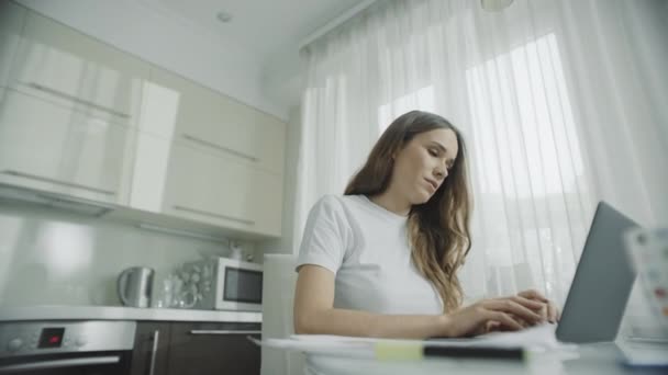Щаслива жінка працює на портативному комп'ютері на кухні. Жінка використовує блокнот — стокове відео
